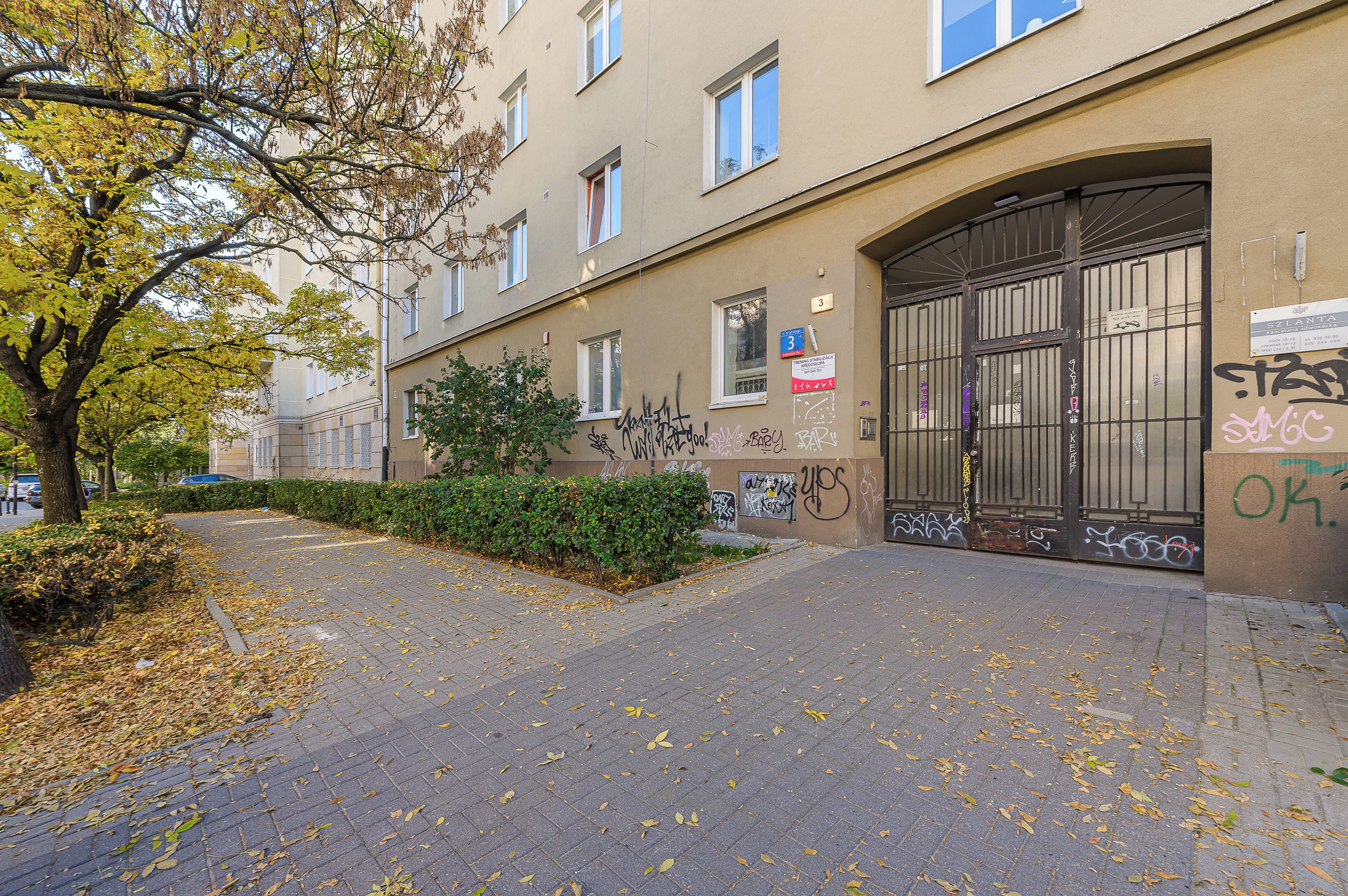 A building with multiple windows, a gated entrance, and some graffiti on the walls.