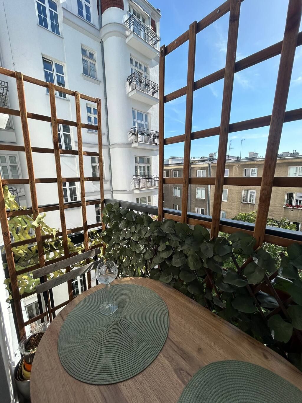 A balcony with a wooden trellis, a round table with a woven placemat, and a potted plant.