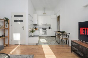 Eine moderne Küche mit weißen Schränken, einem Essbereich mit Tisch und Stühlen sowie einem Fernseher auf einem Schrank.