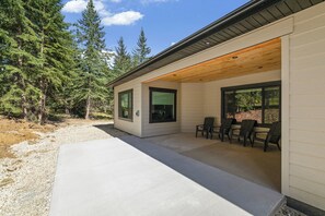 A modern house with a covered patio, large windows, and a view of a forest. - Single Level Property, All King Suites! Access to Community Clubhouse & Pools (Lead)