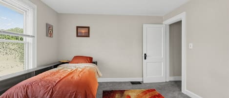 A bedroom with a bed, a window with blinds, a door, and a rug.
