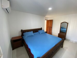 A bedroom with a large bed, wooden headboard, a nightstand, a dresser, a mirror, and a door. - Spectacular apartment with an ocean view (Cartagena de Indias)