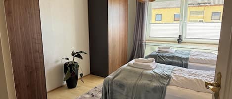 A bedroom with a bed, a hanging light fixture, a potted plant, and a view of the outside.