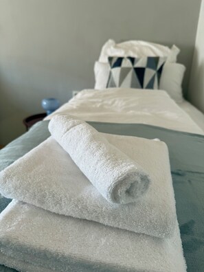 A neatly made bed with a rolled white towel on top, a pillow with a geometric pattern, and a blue pillow.