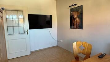 Ein Zimmer mit Holzboden, einem an der Wand befestigten Flachbildfernseher, einem Holzes Esstisch mit Stuhl und einer Tür mit Glasfenster.