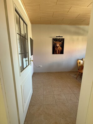 Ein Zimmer mit Fliesenboden, einer Tür mit Fenster und einem an der Wand hängenden Bild.