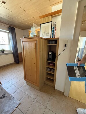 A wooden cabinet with a shelf, a kettle, and a kettle holder on a tiled floor.