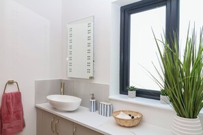 Ein Badezimmer mit einem weißen Waschbecken, einem Spiegel, einem Fenster und einer Topfpflanze.