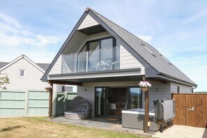 Ein zweistöckiges Haus mit Balkon, Whirlpool und überdachter Sitzgruppe im Freien.
