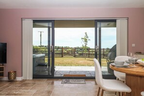 Ein Zimmer mit einer Schiebetür zu einer Terrasse, einem Esstisch mit Geschirr und Gläsern sowie einer durch die Tür sichtbaren Whirlpool-Badewanne.