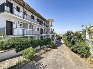 A multi-story building with balconies, a paved driveway, and surrounding greenery. - SANTA CATALINA Rosas / Roses – INTERimmo (Rosas / Roses)