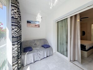 A room with a grey sofa, two blue cushions, a painting of a beach, and a sliding glass door leading to another room. - SANTA CATALINA Rosas / Roses – INTERimmo (Rosas / Roses)