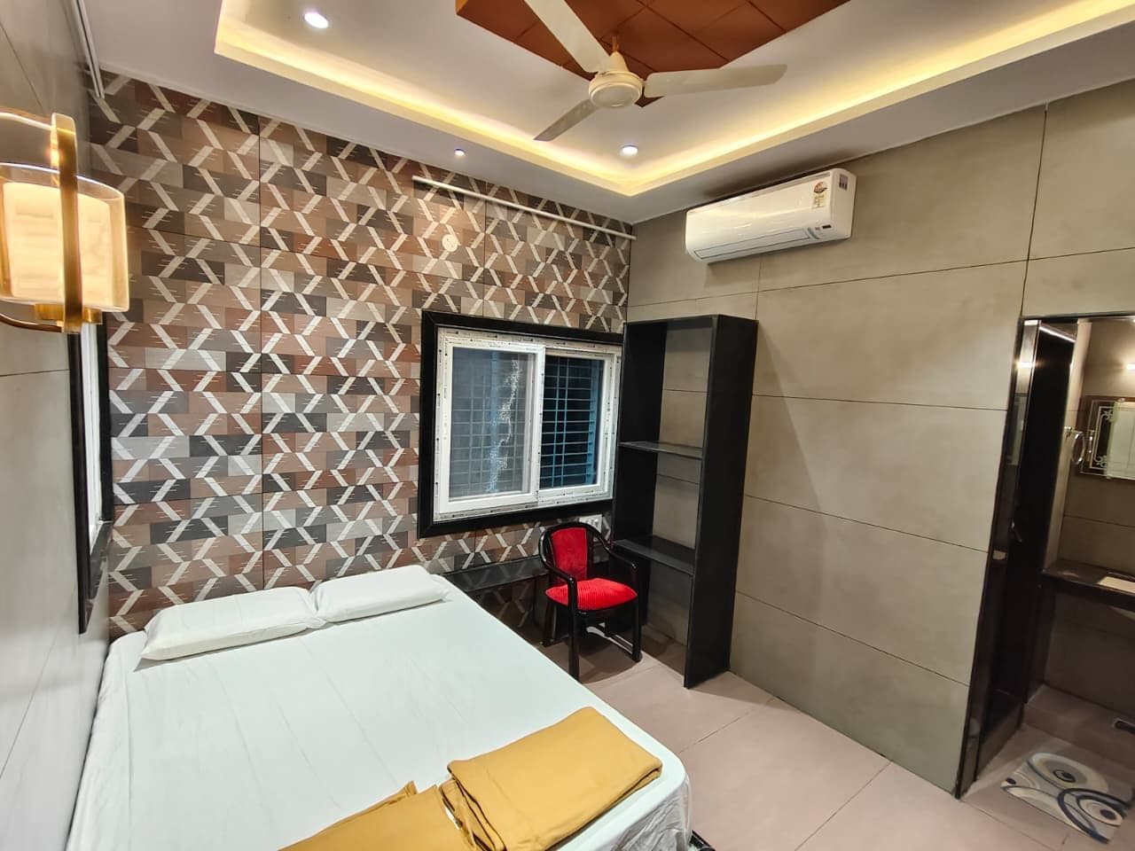 A bedroom with a bed, a window, a red chair, a wardrobe, and an air conditioning unit.