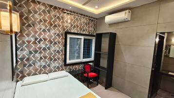 A bedroom with a bed, a window, a red chair, a wardrobe, and an air conditioning unit.