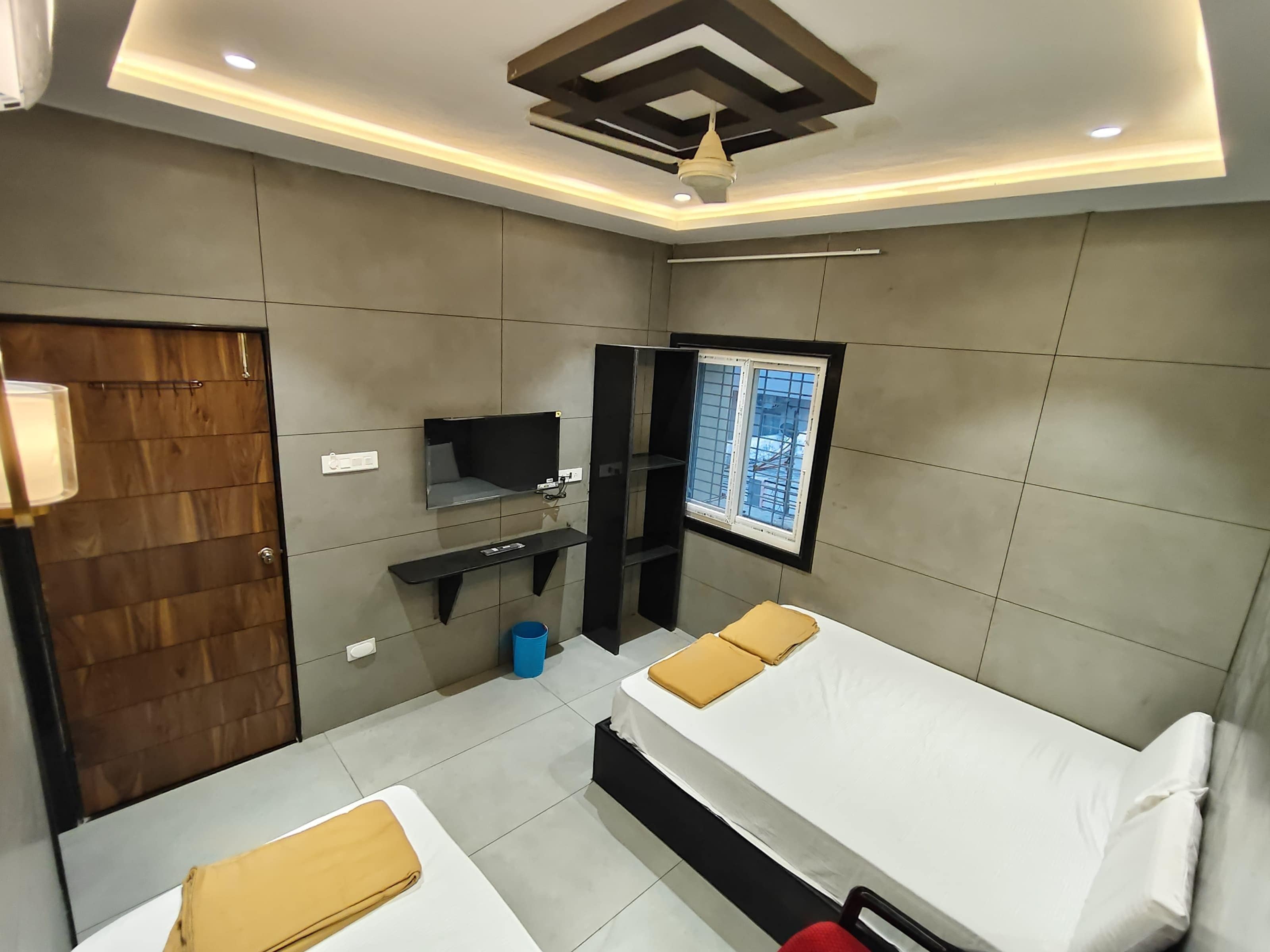 A modern hotel room with two beds, a TV, a window, and a ceiling light fixture.