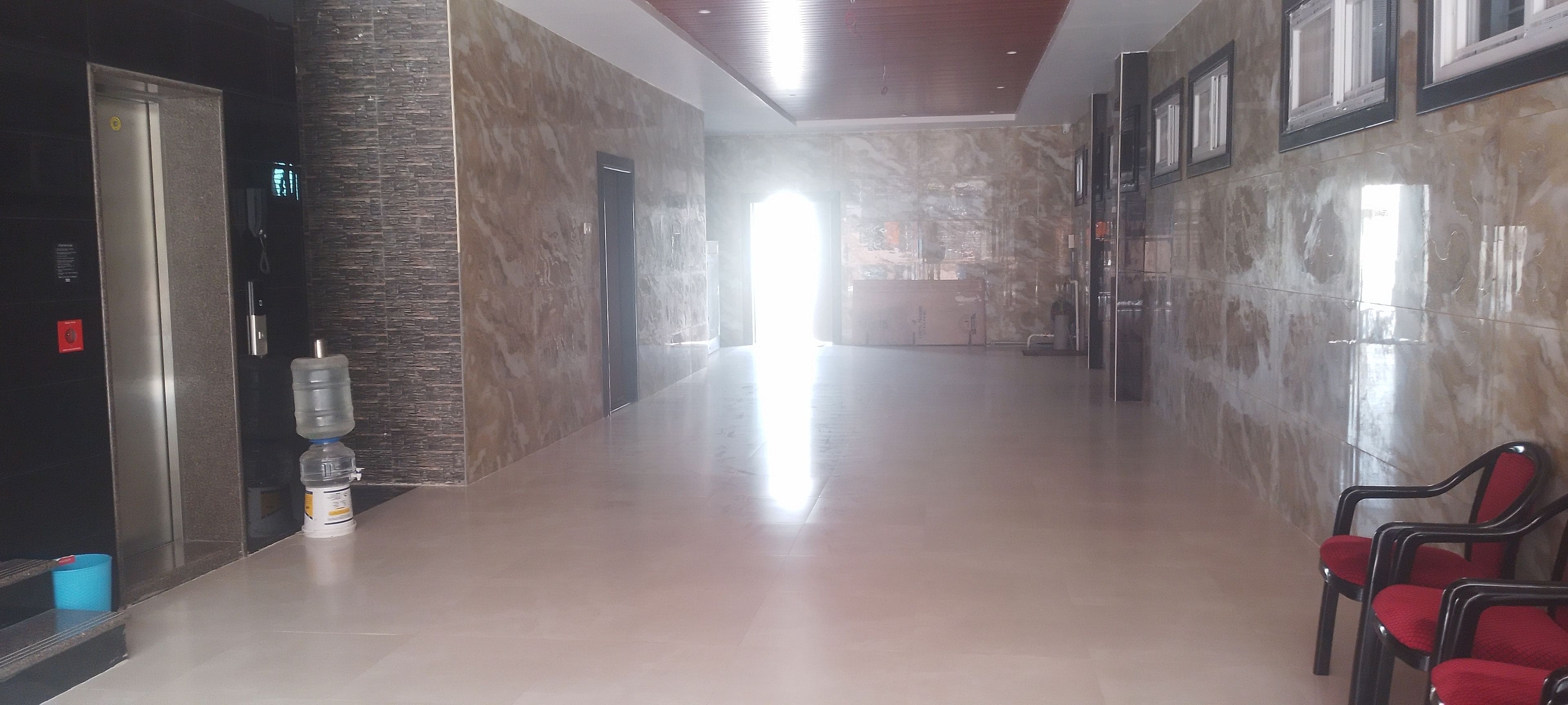 A hotel lobby with a marble floor, a reception desk, and red chairs.
