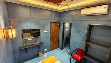 A compact hotel room with a bed, a TV, a wardrobe, a chair, and a shelf.