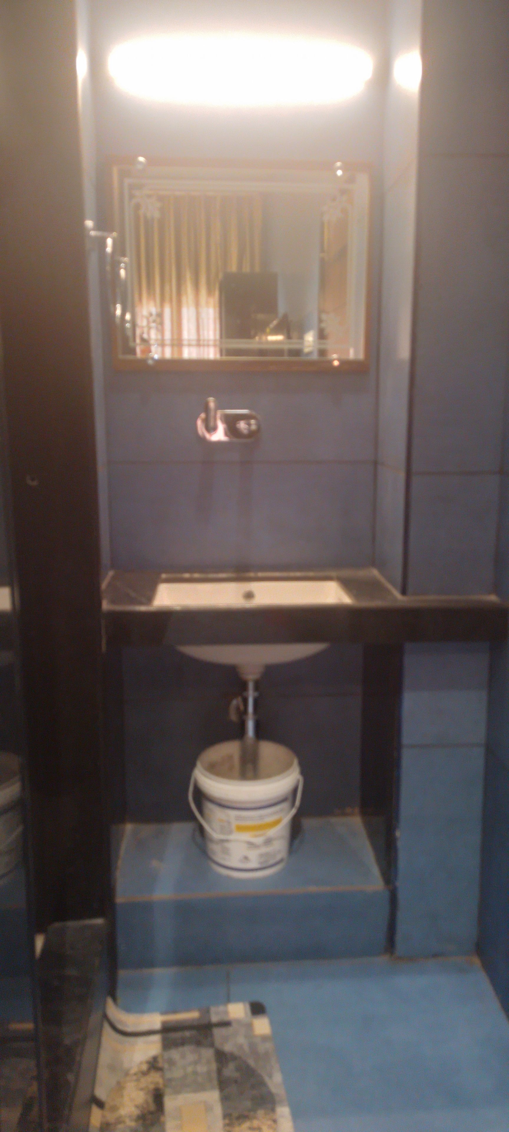 A bathroom with a sink, mirror, and a bucket under the counter.