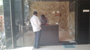 Un área de recepción con pared de mármol, mostrador de recepción y puerta de cristal.