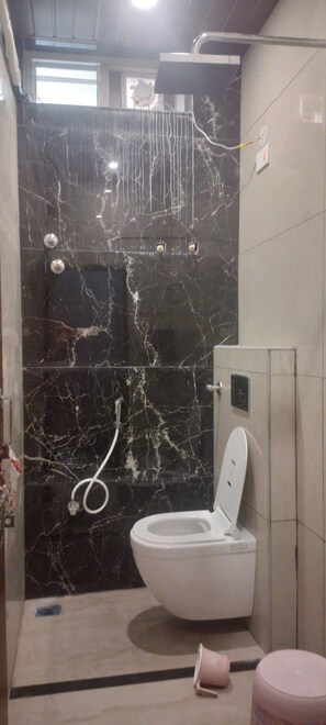 A bathroom with a toilet, a shower, and a marble wall. - Srivara Grand Mantralayam  (Mantralayam)