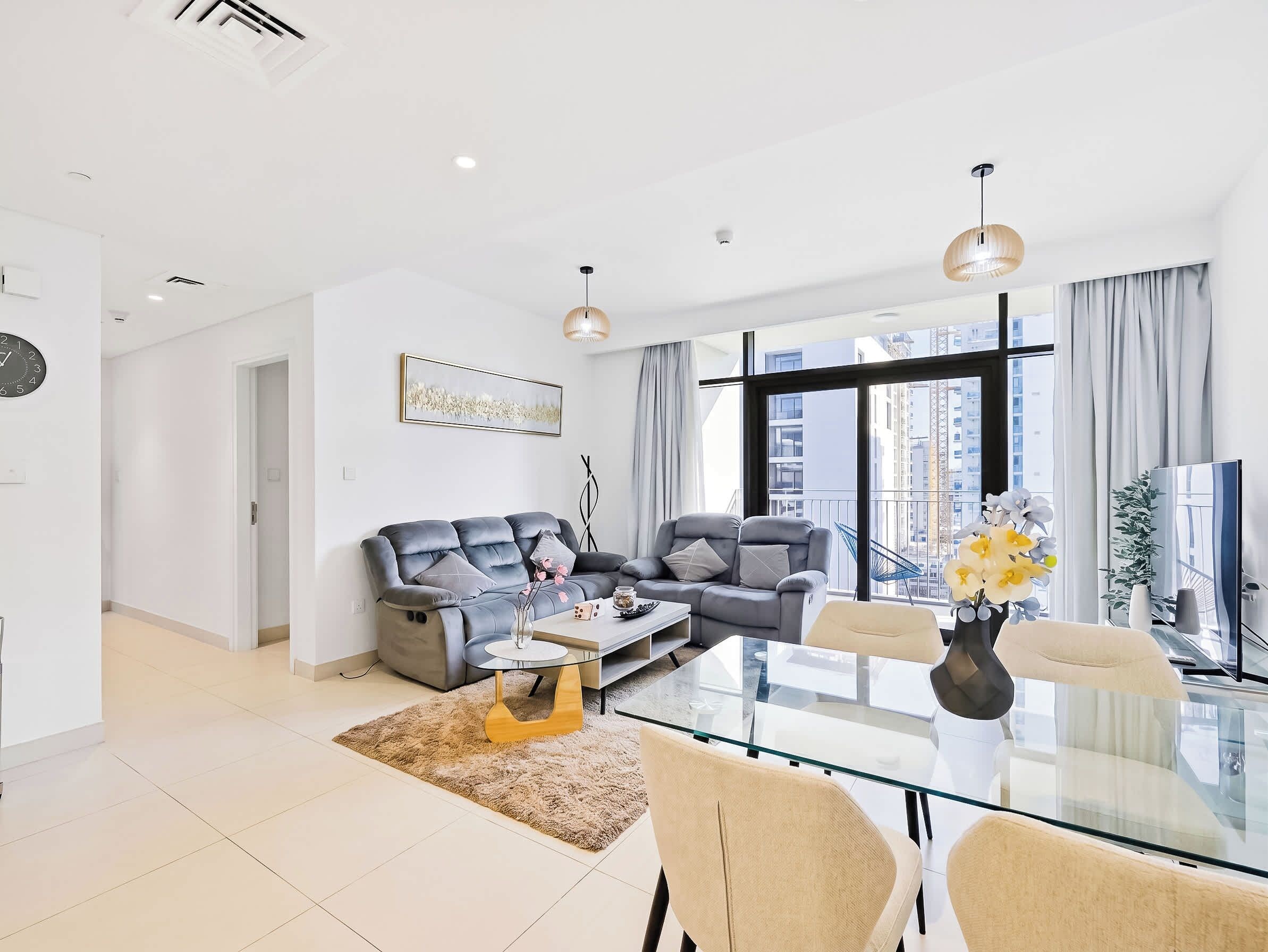 A modern living room with a sofa, armchairs, a glass coffee table, and a view of the city through large windows.