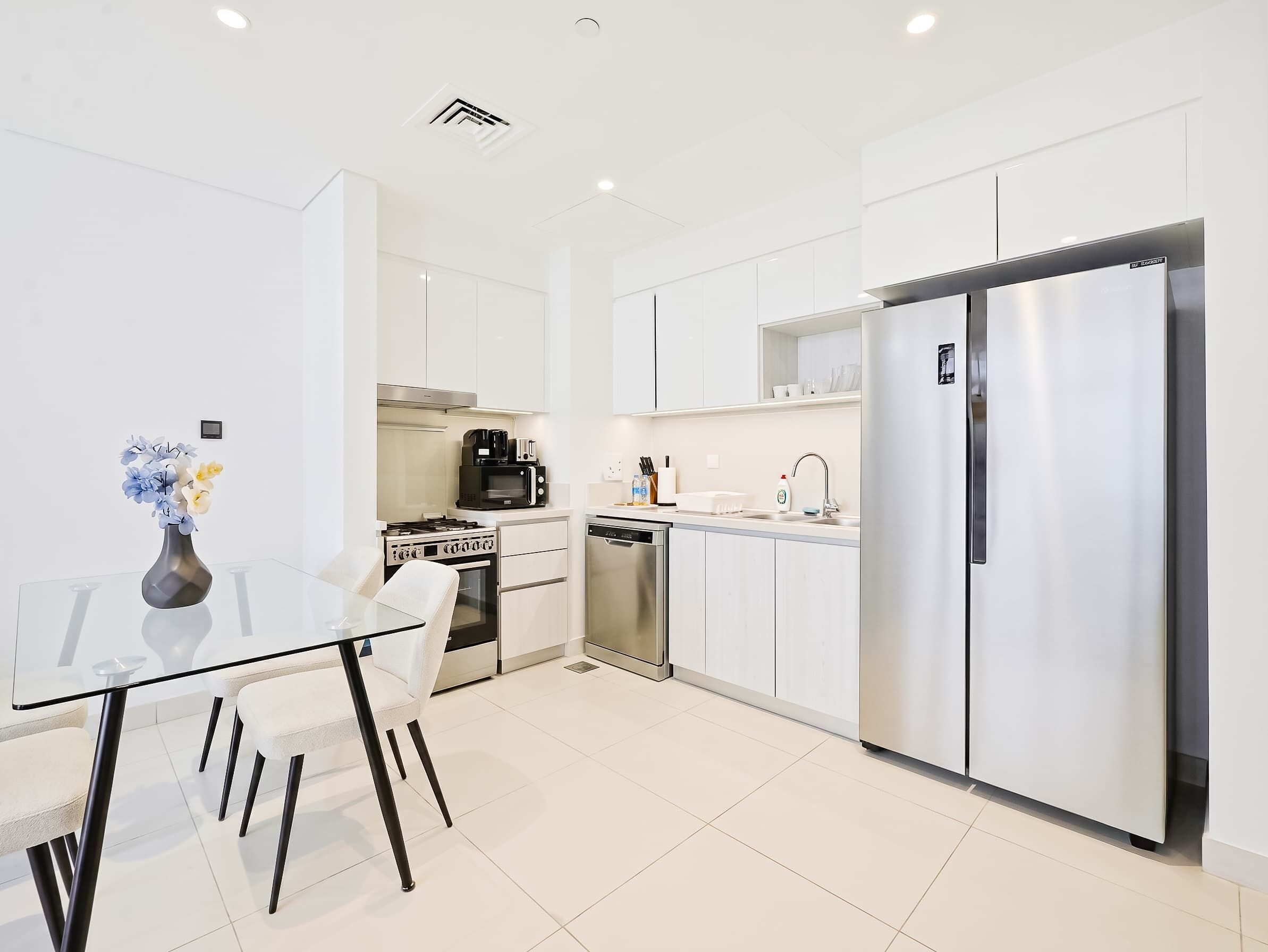 A modern kitchen with white cabinetry, stainless steel appliances, and a glass dining table.