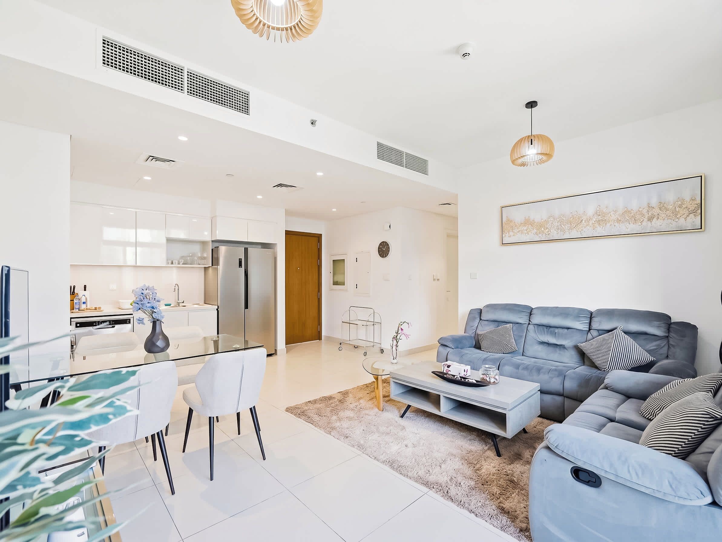 A modern living room with a grey sofa, a coffee table, and a dining area with a glass table and chairs.
