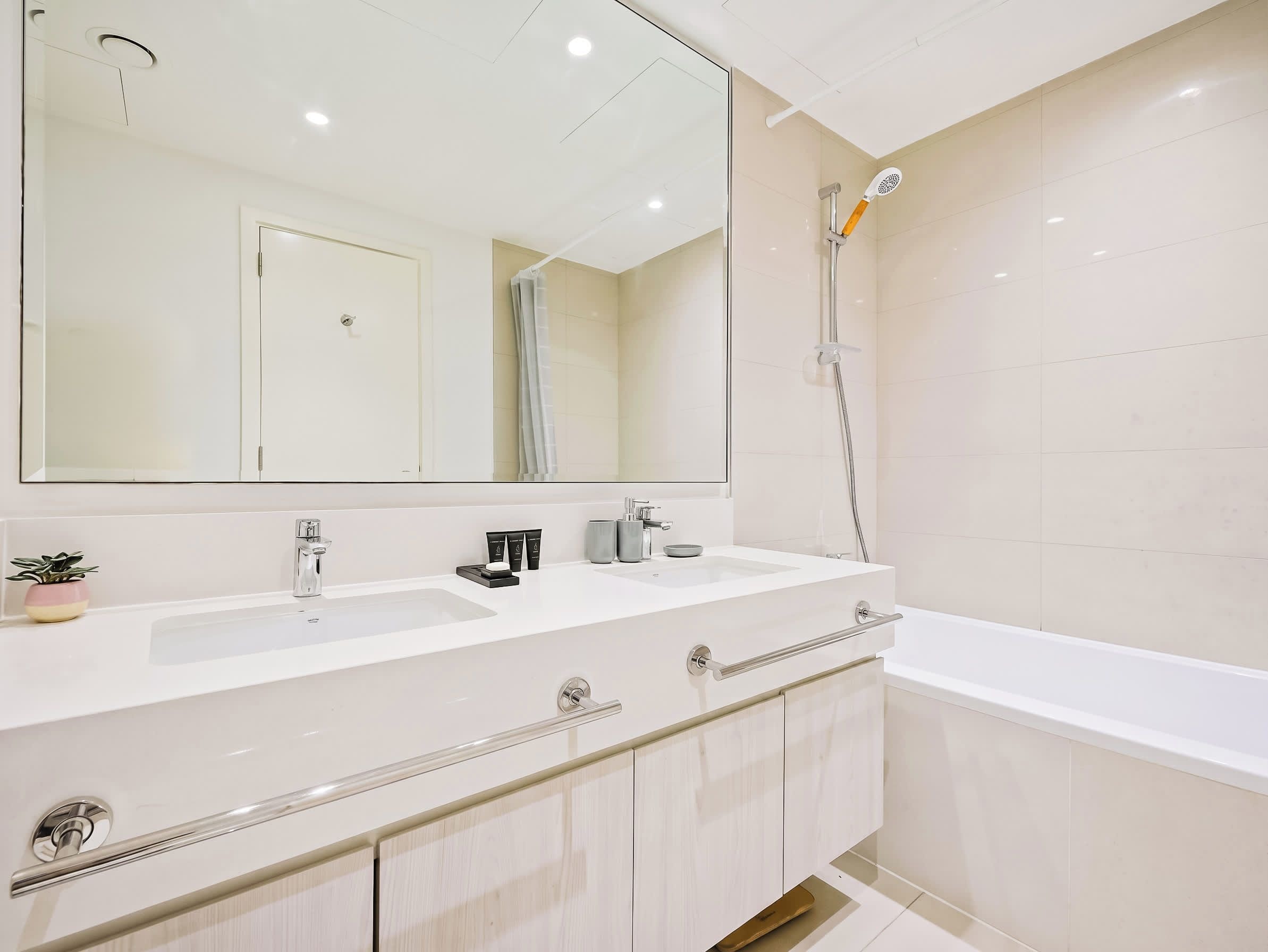 Une salle de bain moderne avec un meuble-lavabo à deux vasques, un grand miroir, une douche avec un pommeau de douche à main et une baignoire.