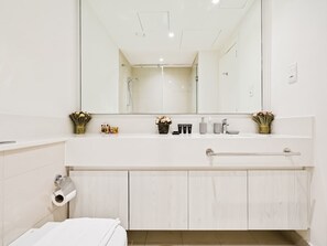 Ein modernes Badezimmer mit einem großen Spiegel, einer Toilette und einem Waschbeckenbereich mit Pflegeprodukten.