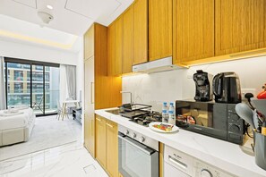 A modern kitchen with wooden cabinets, a built-in oven, and a coffee machine. - Riviera 59 Studio · Lagoon · Meydan (Dubai)