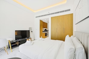 A modern hotel room with a large bed, a flat-screen TV, a desk, and a kitchenette. - Riviera 59 Studio · Lagoon · Meydan (Dubai)