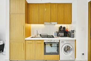 A compact kitchen with wooden cabinets, a built-in oven, a dishwasher, and a coffee machine. - Riviera 59 Studio · Lagoon · Meydan (Dubai)