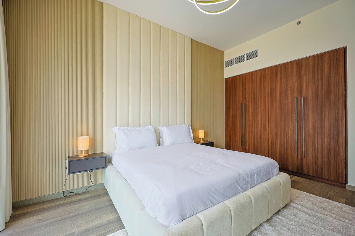 Quarto moderno com cama grande, abajures, guarda-roupa e radiador.