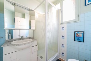 Ein Badezimmer mit Duschkabine aus Glas, einem Waschbecken mit Marmorplatte und einer wandmontierten Toilette.