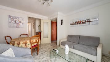 Una sala de estar con un sofá gris, una mesa de centro de vidrio, una mesa de comedor con sillas y obras de arte en las paredes.