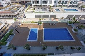 A rooftop swimming pool area with two pools, surrounded by lounge chairs and potted plants. - Azizi 63 Studio · Pool & Gym · Meydan (Dubai)