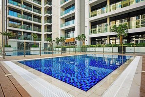 A modern building with a rectangular pool surrounded by a wooden deck. - Azizi 63 Studio · Pool & Gym · Meydan (Dubai)
