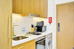 A compact kitchen with a sink, stove, microwave, and a washing machine. - Azizi 63 Studio · Pool & Gym · Meydan (Dubai)