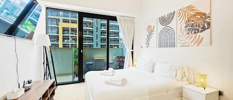 A modern hotel room with a large bed, a desk, a flat-screen TV, and a balcony with a view of the city.