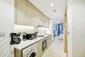 A modern kitchen with a built-in washing machine, a coffee maker, and a microwave. - Riviera 42 Studio · Lagoon Resort · Meydan (Dubai)