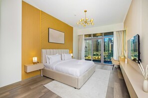 A modern hotel room with a large bed, a nightstand, a chandelier, a large window with a city view, and a flat-screen TV. - Imperial 2BR · Burj View · Downtown (Dubai)