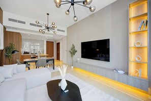 A modern living room with a large flat-screen TV, a black coffee table, and a bookshelf with books. - Imperial 2BR · Burj View · Downtown (Dubai)