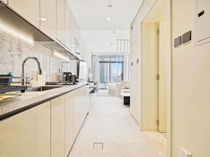 A modern kitchen with a marble countertop, stainless steel appliances, and a view of a cityscape through large windows. - Modern Studio Escape - Relax & Unwind (Dubai)