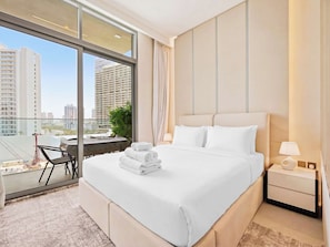 A hotel room with a large bed, a nightstand, a lamp, and a view of tall buildings through the window. - Modern Studio Escape - Relax & Unwind (Dubai)