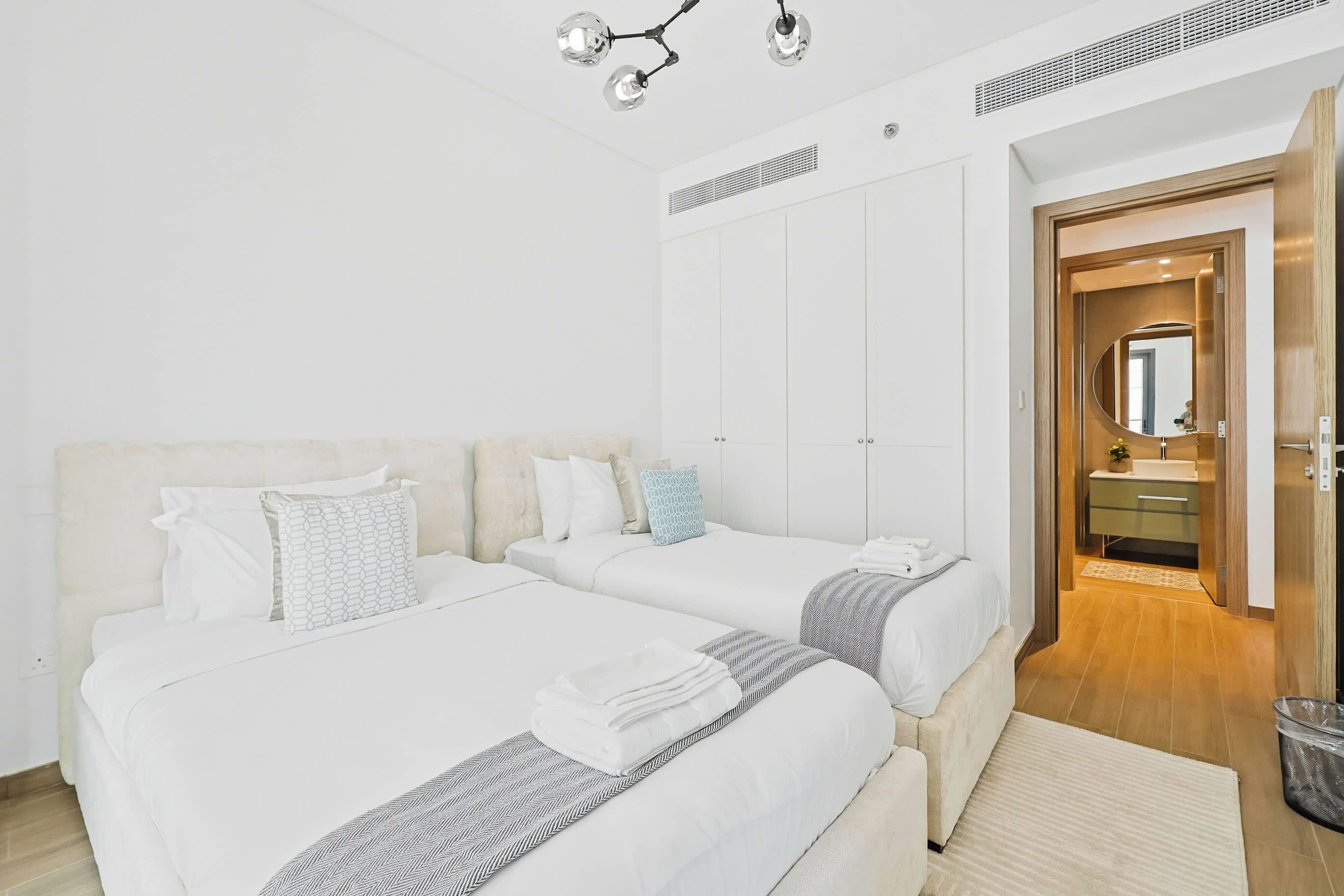 A hotel room with two beds, a bathroom with a mirror, and a wooden floor.