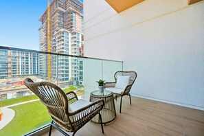 Un balcon doté de meubles en osier, d’une table en verre et offrant une vue sur un immeuble de grande hauteur en construction.