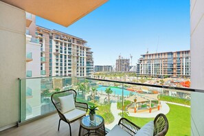 Un balcon agrémenté de meubles en osier, d’une table en verre et offrant une vue sur une piscine et les bâtiments environnants.