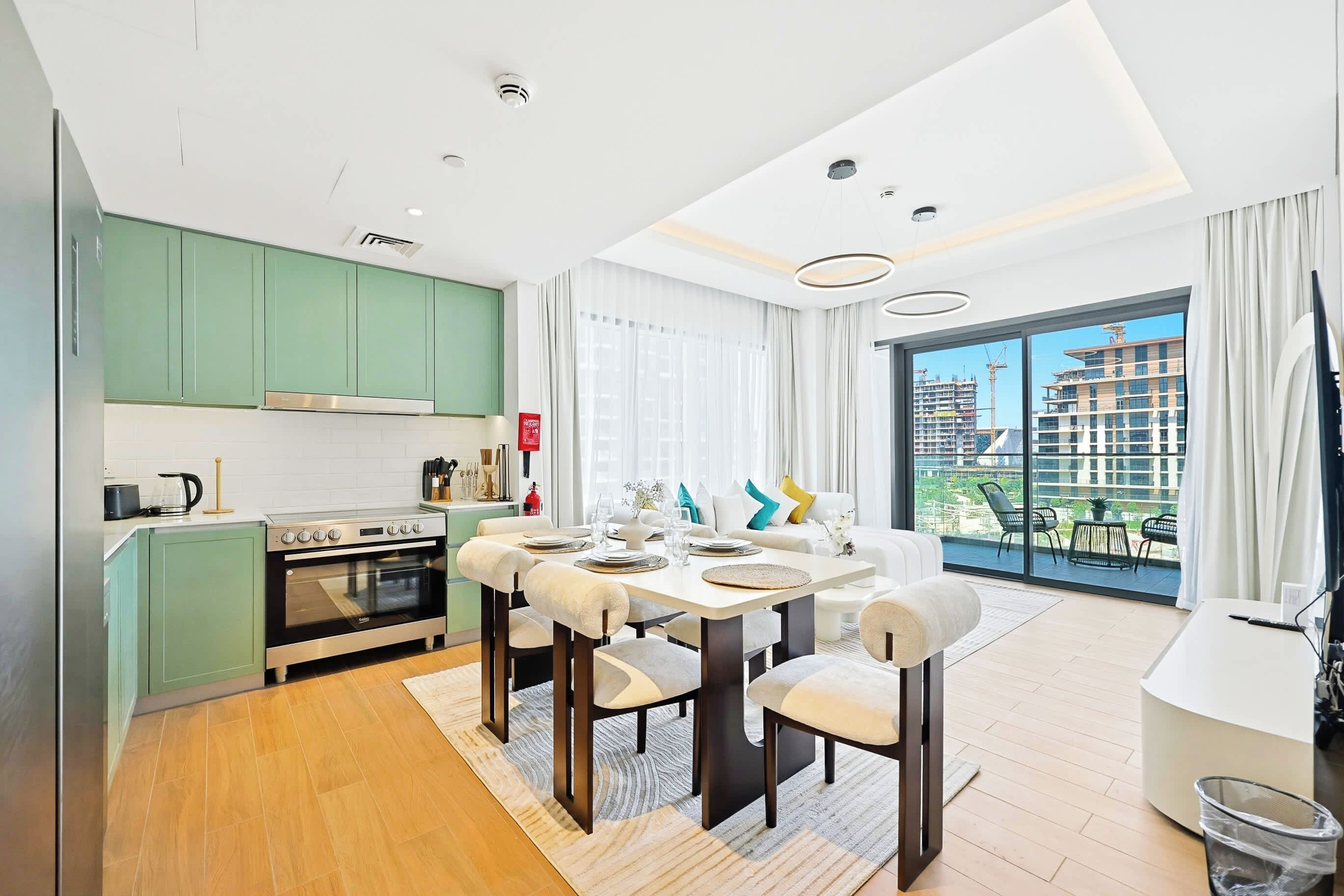 A modern kitchen with green cabinets, a built-in oven, and a dining area with a table set for four.