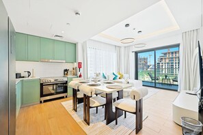 A modern kitchen with green cabinets, a built-in oven, and a dining area with a table set for four. - Celadon 2BR · City Walk · Pool & Gym (Dubai)