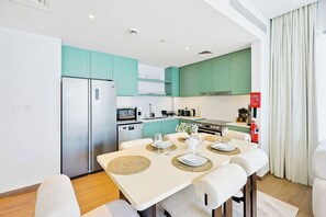 A modern kitchen with teal cabinets, a stainless steel refrigerator, and a dining area with a table set for two. - Celadon 2BR · City Walk · Pool & Gym (Dubai)